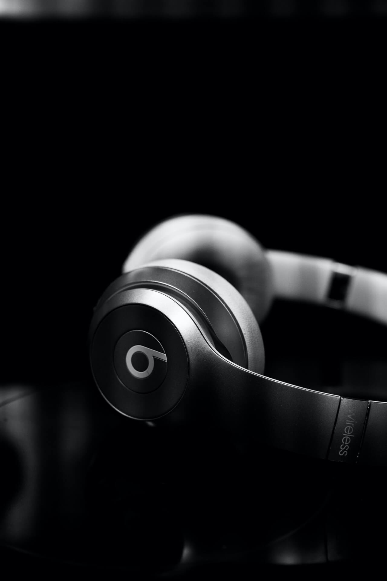 Black and white image of Beats headphones resting on a reflective surface, viewed from the side.