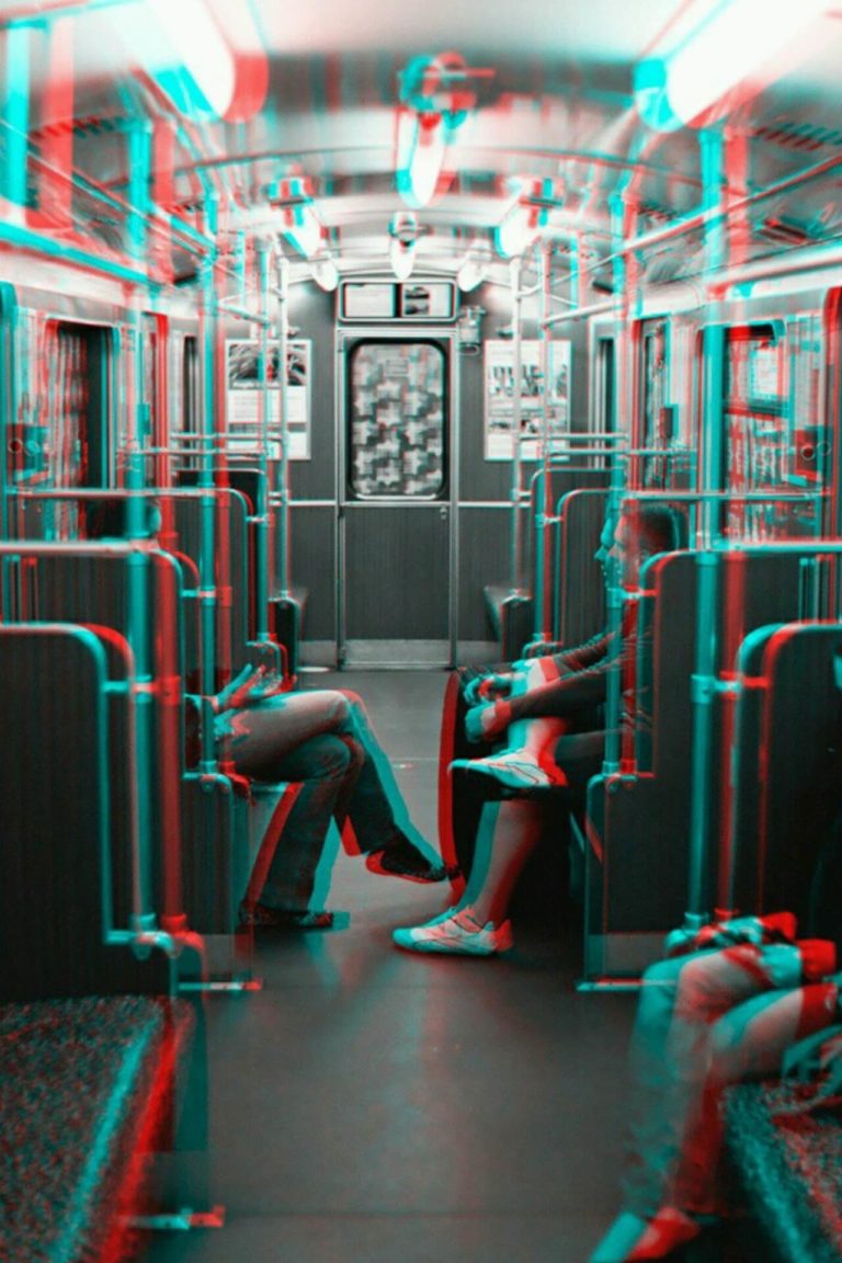 A 3D anaglyph image of a subway car interior with several passengers seated. The scene has a red and blue double image effect typical of 3D anaglyphs.