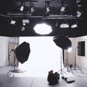 Photography studio setup with a bright backdrop, multiple lighting umbrellas, and equipment on the floor.