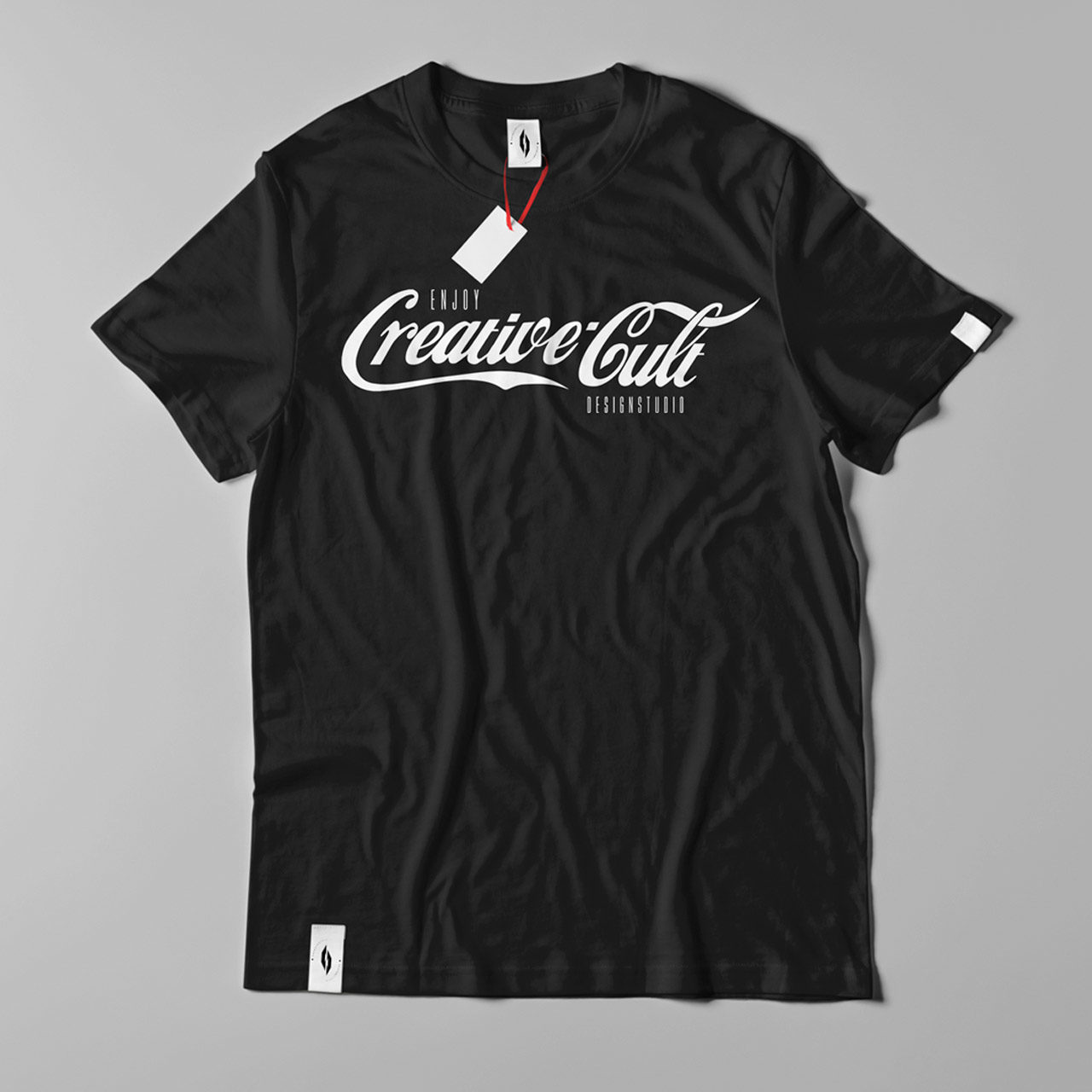 Black t-shirt with "Creative Cult" written in cursive white text. A tag is attached to the neckline with a red string. The shirt is displayed on a flat, light gray background.