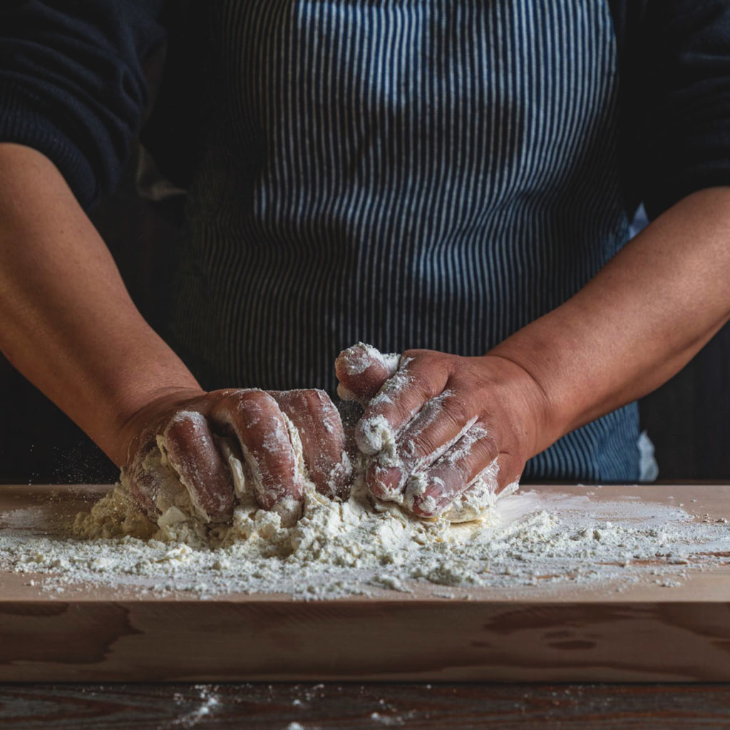 Person kneading dough with flour on a wooden board, wearing a striped apron.