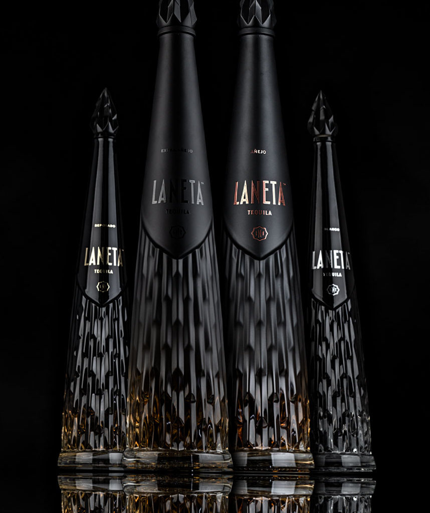 Four elegant black bottles of Laneta tequila are arranged against a dark background, showcasing different sizes and styles.