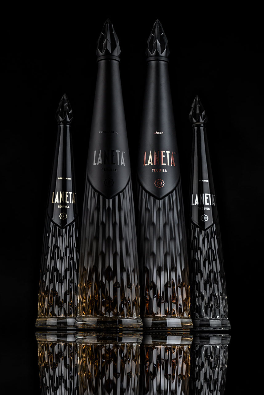 Four elegant black bottles of Laneta tequila are arranged against a dark background, showcasing different sizes and styles.