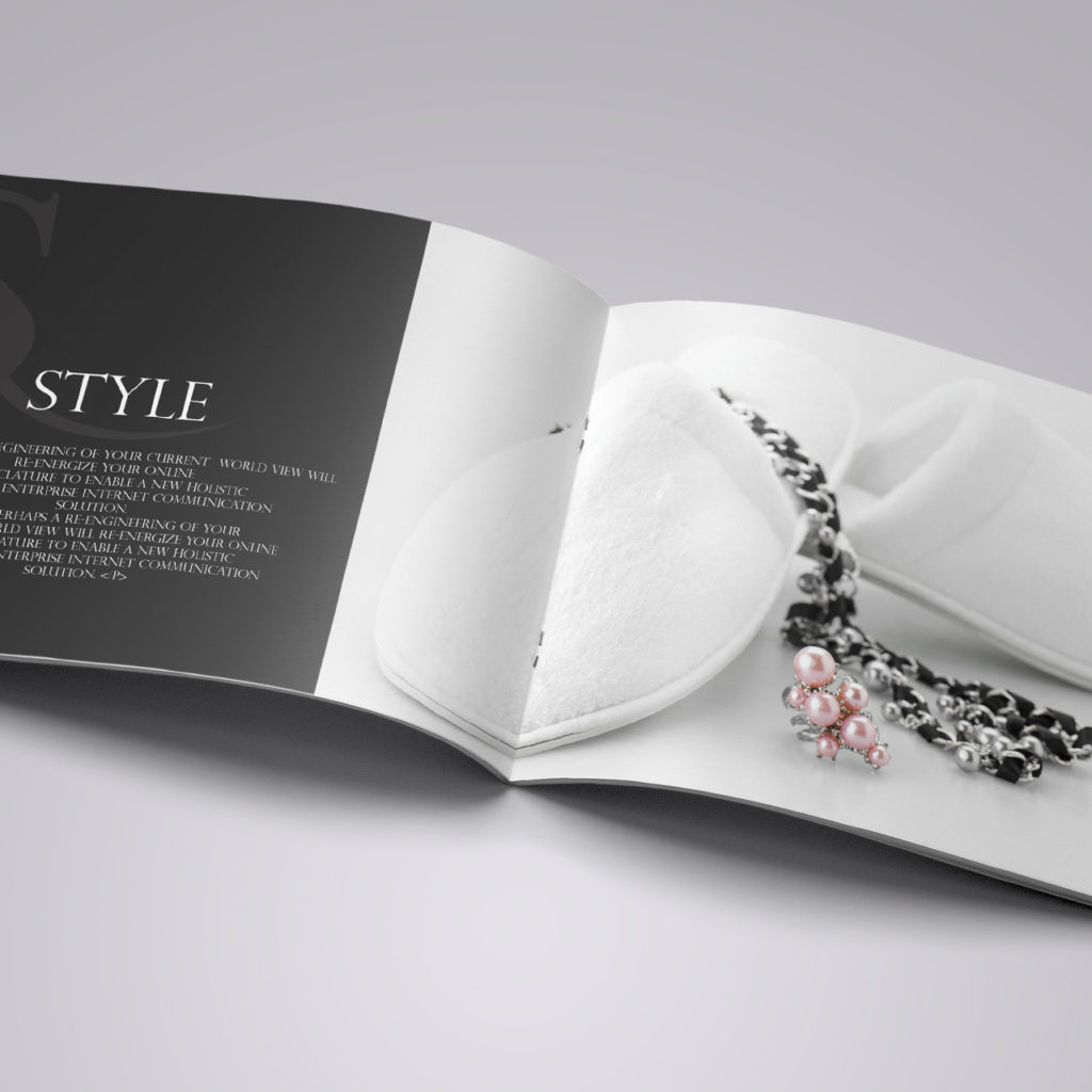 Open brochure featuring a black and white page on the left with the word "Style" and fashion text, and a right page with white slippers and a chain necklace with pearls.